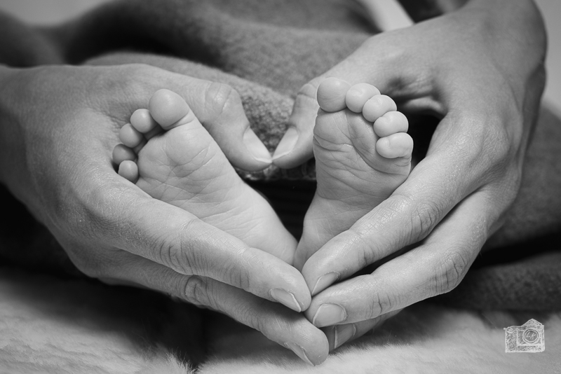 Mutter hält Babyfüße, dabei formt die Mutter mit ihren Händen ein Herz. Schwarzweiß-Bild.